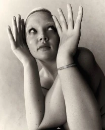 Close up portrait of a blonde woman holding her hands up near her face wearing a silver bracelet