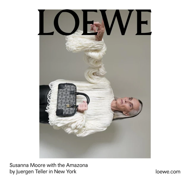 Fashion shot featuring mature woman with white hair wrapped in cream fringe, holding patterned purse in a light grey studio setting.