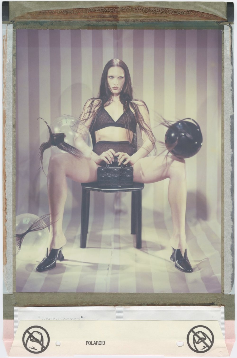 Stylish portrait of a woman in lingerie and high heels sitting on a stool indoors in front of a striped wall with balloons.