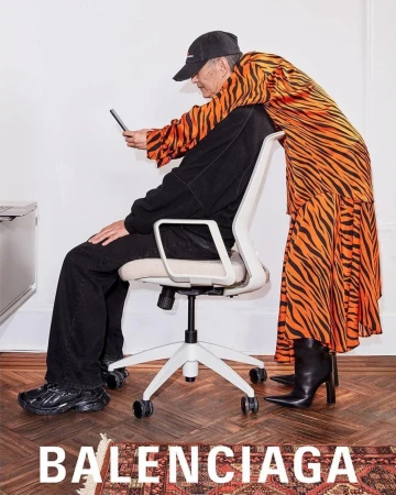 Fashion editorial featuring an adult female in an orange tiger-striped dress and an adult male in a black tracksuit in a studio.