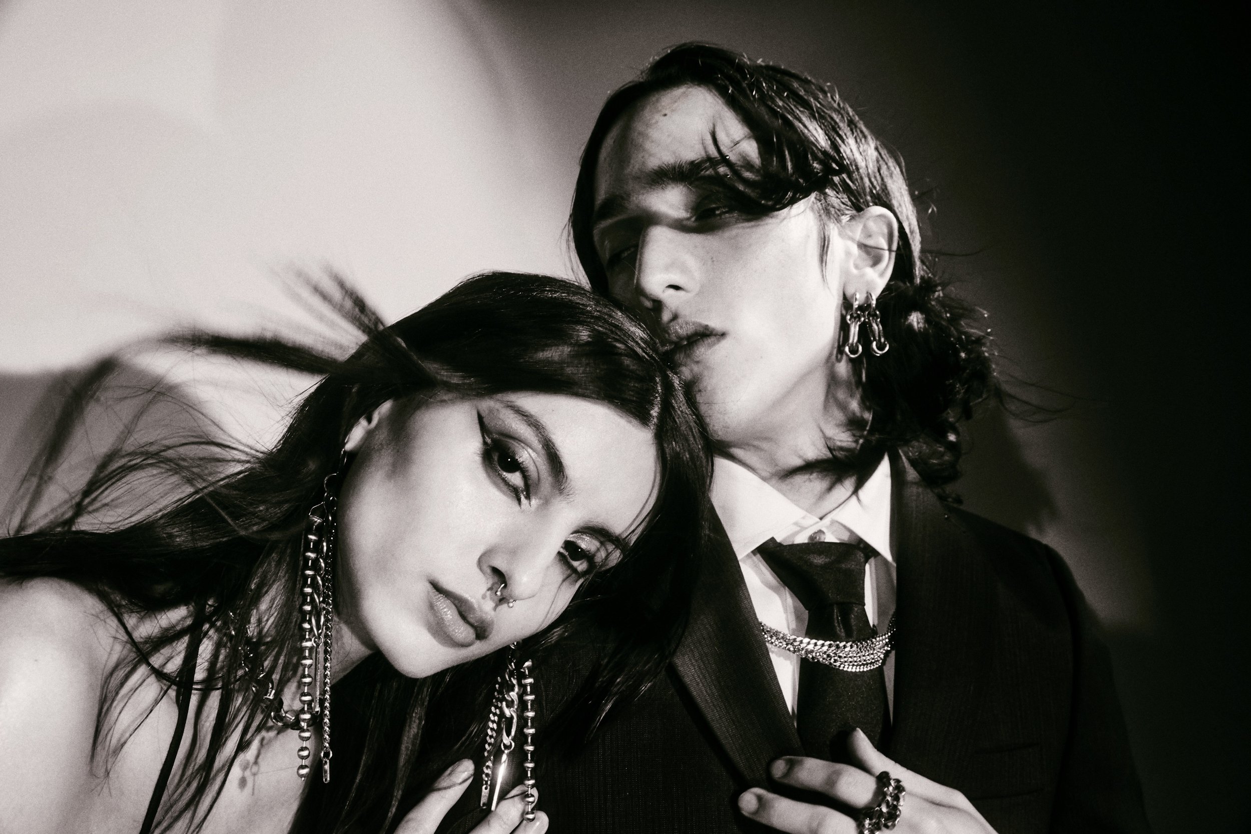 Monochrome portrait of a fashionable couple, a woman with dramatic eye makeup and a man in a suit, posing in a studio setting.