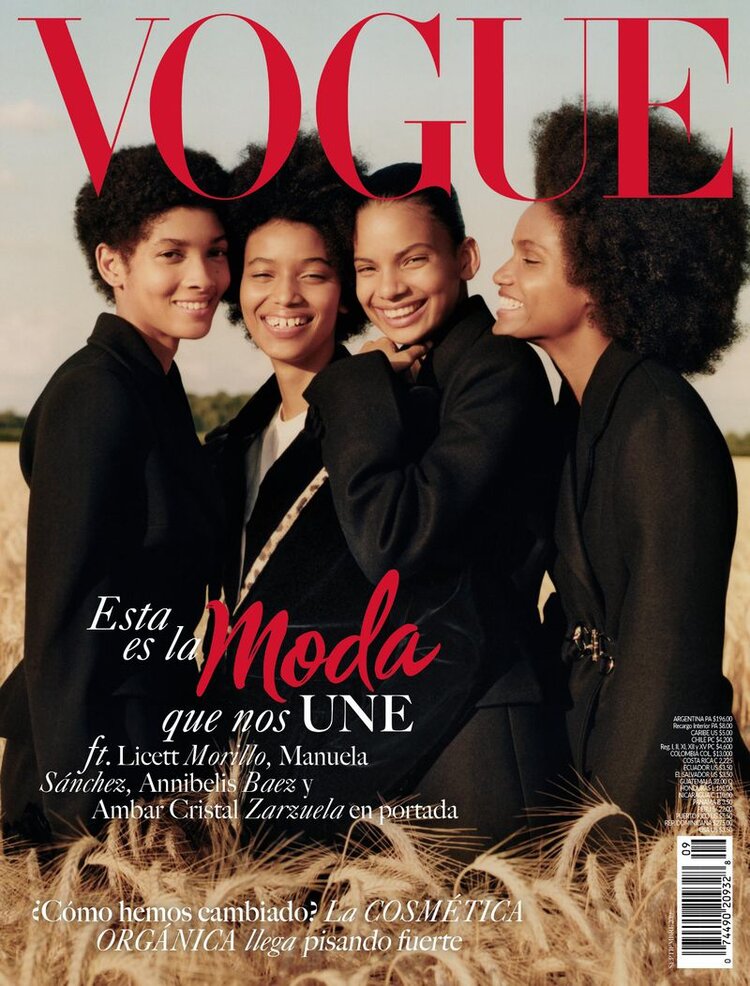 Vogue magazine cover featuring four smiling women with afro hairstyles wearing black blazers standing in a wheat field under the Vogue logo.