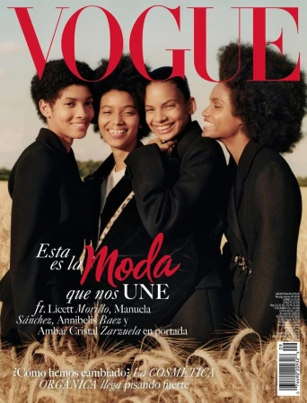 Vogue magazine cover featuring four smiling women with afro hairstyles wearing black blazers standing in a wheat field under the Vogue logo.