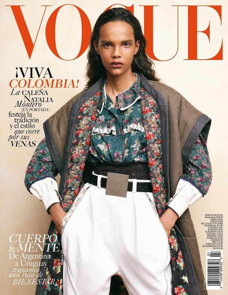 Vogue magazine cover featuring a model in floral top, white pants, and a brown jacket, posing against a neutral background. Bold red masthead.