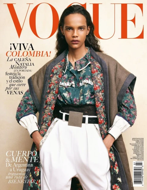Vogue magazine cover featuring a model in floral top, white pants, and a brown jacket, posing against a neutral background. Bold red masthead.