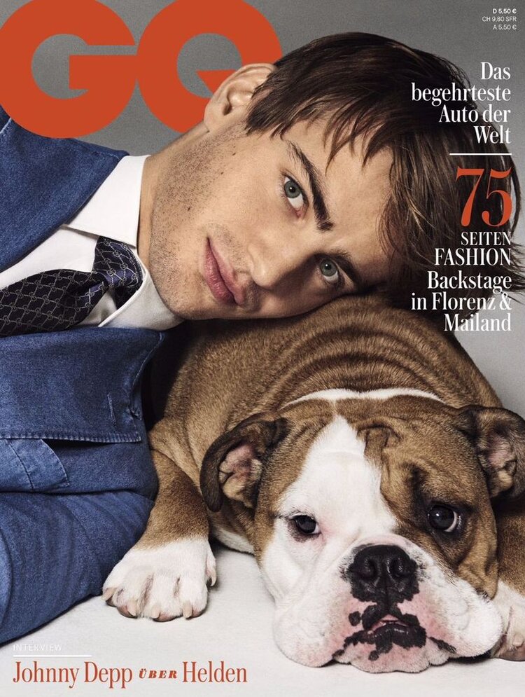 GQ magazine cover featuring a handsome adult male resting his head on an English Bulldog, wearing a blue suit and tie in a photo studio.