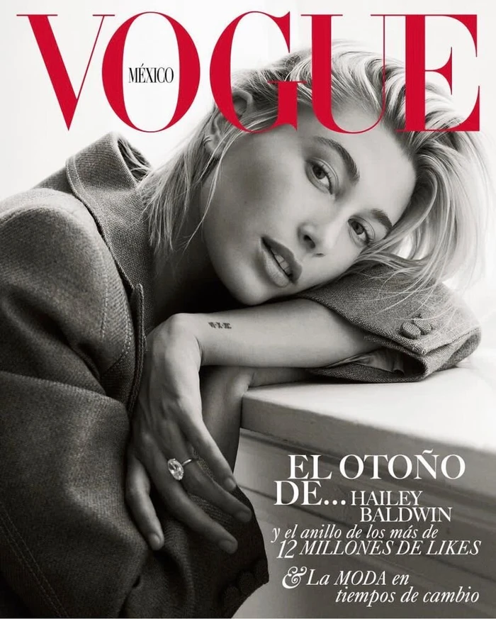 Close-up portrait of Hailey Bieber resting her head on her arm, wearing a grey blazer and a large diamond ring, Vogue Mexico cover.
