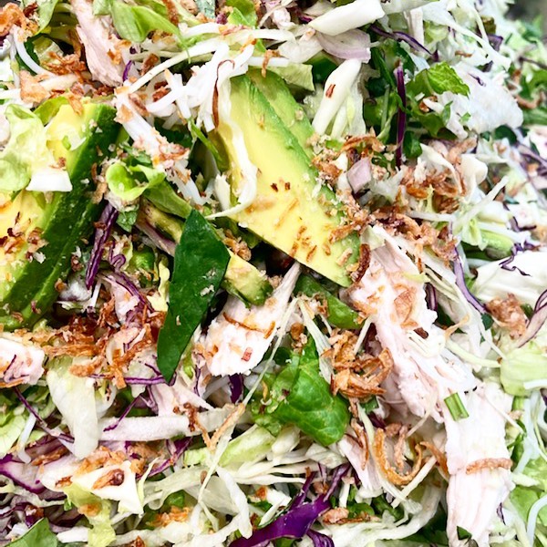 Overhead shot of a vibrant salad featuring fresh lettuce, avocado slices, shredded cabbage, and crispy fried onions as a topping.