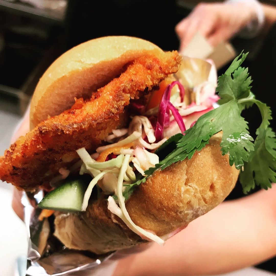 Close-up of a banh mi sandwich featuring a crispy fried cutlet, fresh cilantro, shredded cabbage, and cucumber slices.