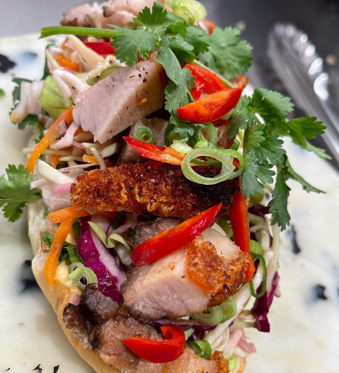Close-up of a banh mi sandwich featuring grilled pork, vibrant vegetables, cilantro, and crusty bread. Food and beverage photography.