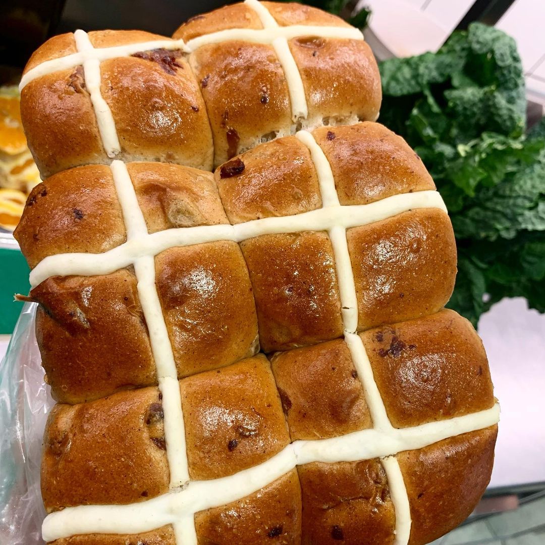 Close-up of freshly baked hot cross buns with a white cross design, showcasing their golden crust and inviting texture for Food and Beverage.