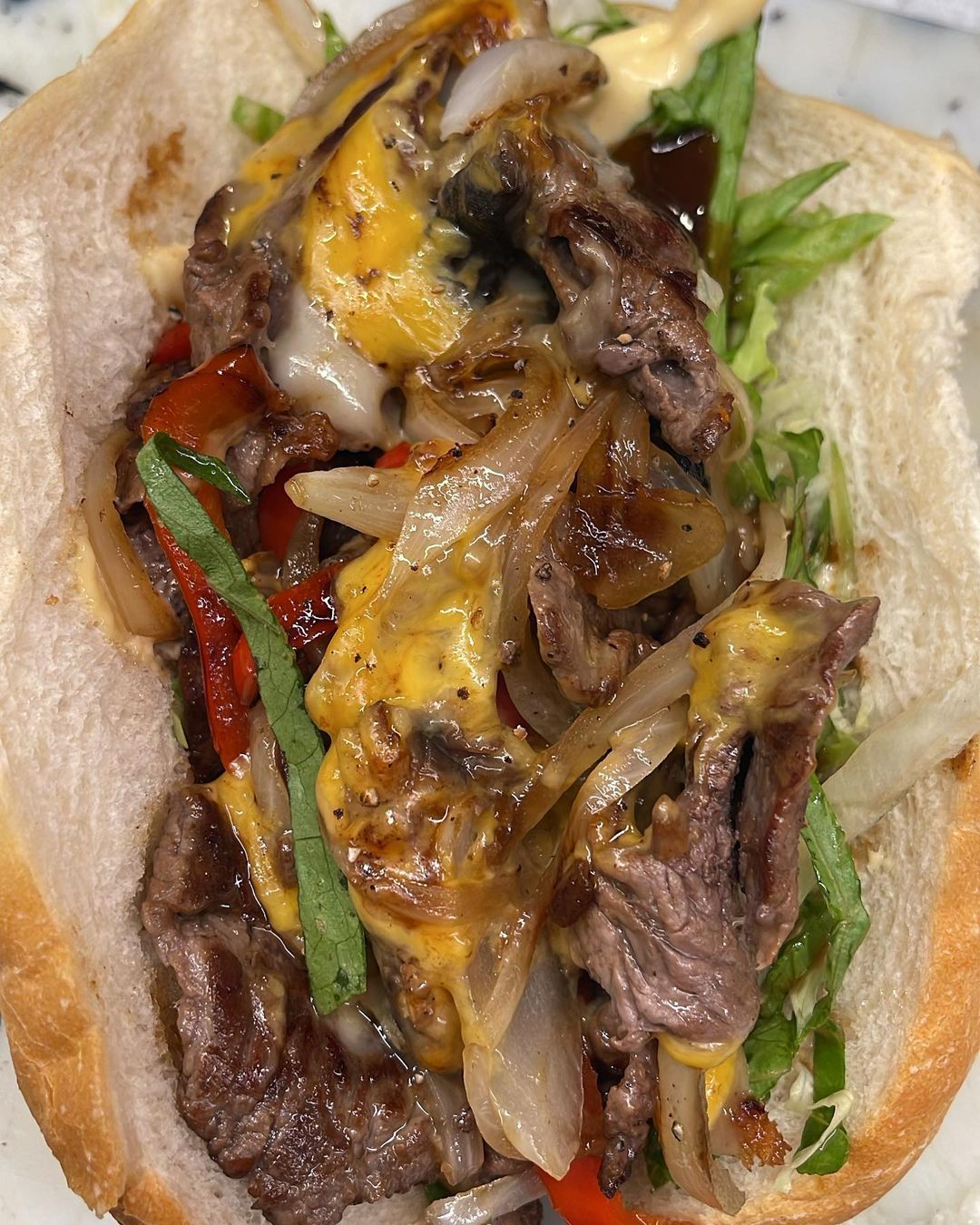 Delicious Philly cheesesteak sandwich on a white bun filled with sliced beef, melted cheese, grilled onions, peppers, and lettuce.