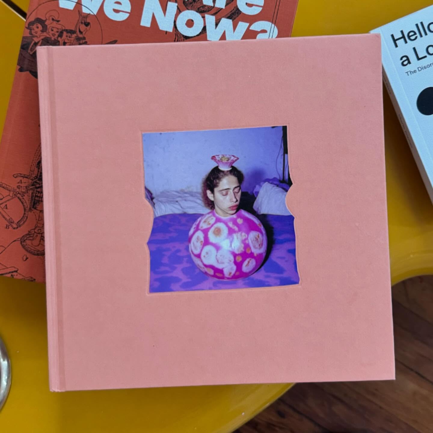 Pink square book with a central die-cut window displaying an image of a person inside a patterned pink sphere.