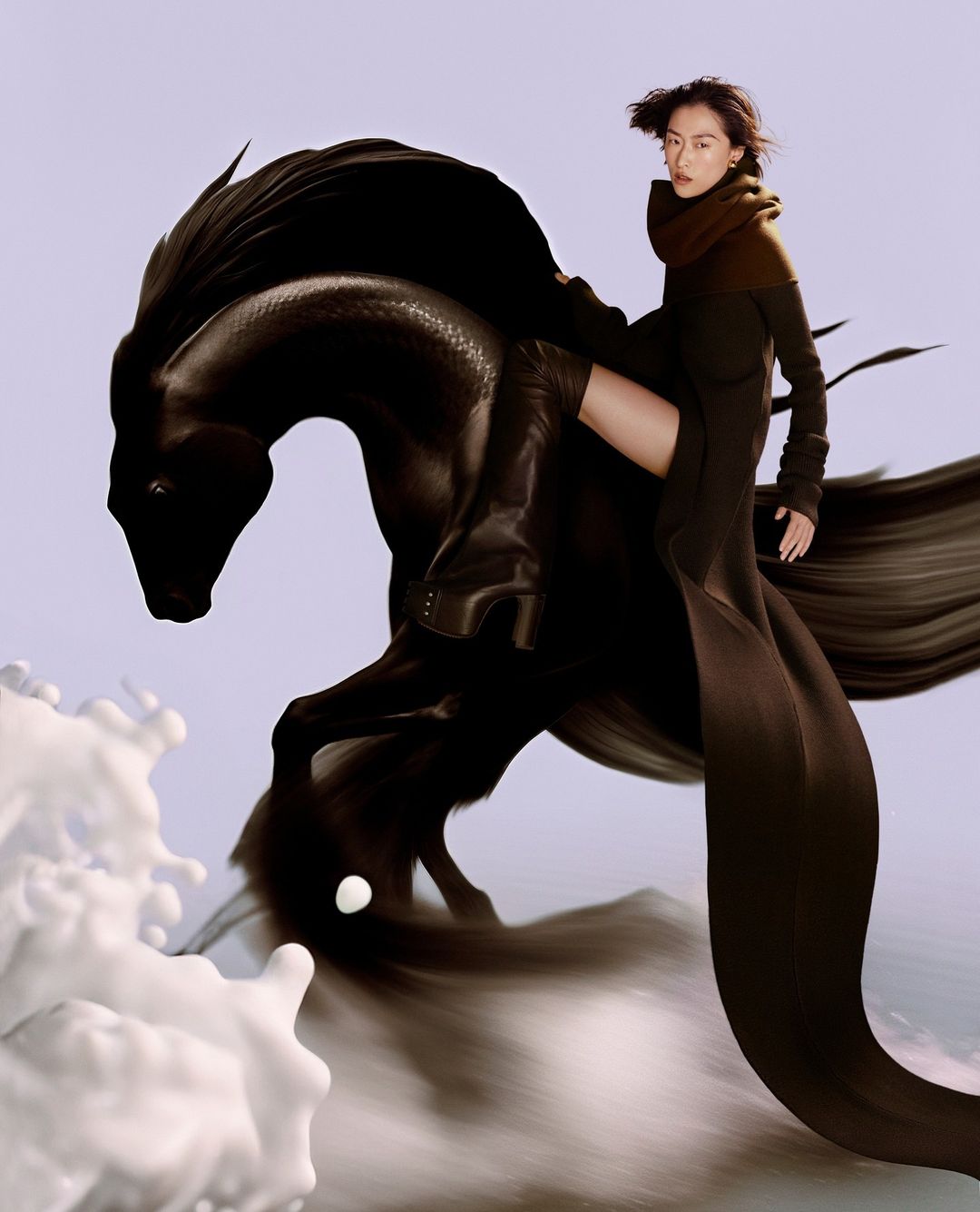Woman in dark long coat and thigh-high boots riding a surreal black horse sculpture with white splashing waves.