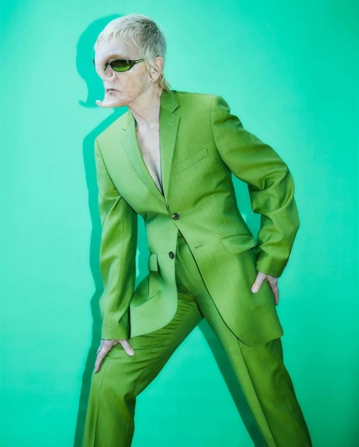 Portrait of an adult wearing a vivid green suit and matching sunglasses, set against a bright green background.