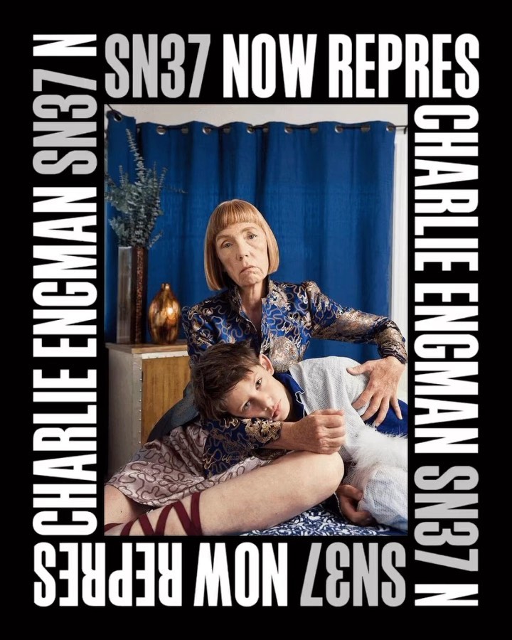 Older and younger adult embrace indoors. A blue curtain backdrop and surrounding advertisement text frame the subjects.