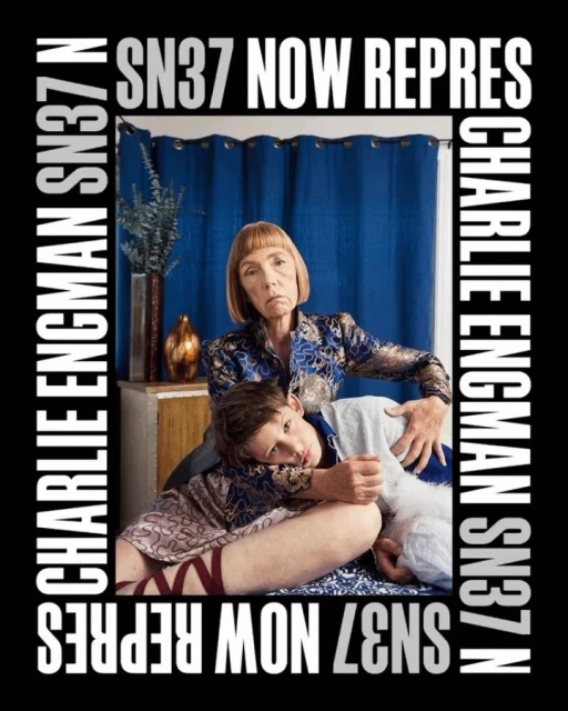 Older and younger adult embrace indoors. A blue curtain backdrop and surrounding advertisement text frame the subjects.