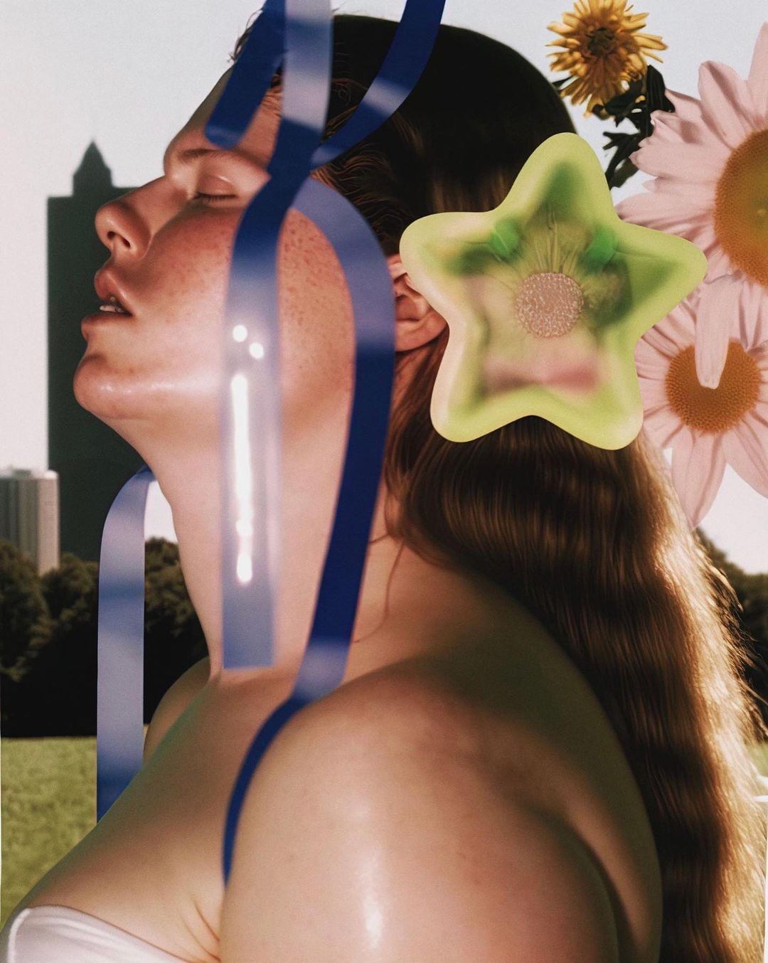 Woman in close-up shot with long brown hair, star-shaped hair accessory, flowers, and blue ribbon in an outdoor park setting.