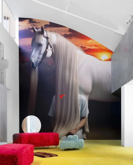 Interior with a large mural of a white horse behind furniture and a person whose face is obscured by the horse's mane.