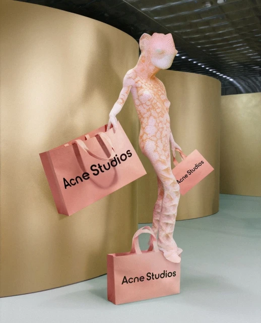 Art installation with a mannequin holding shopping bags that feature the text “Acne Studios” against a gold and teal background.