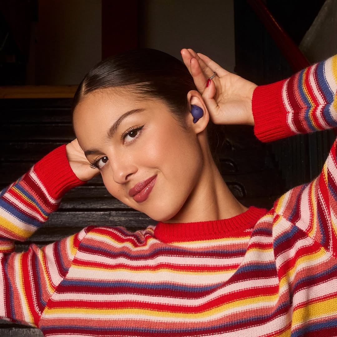 A portrait captures a woman with brown hair and a colorful striped sweater, posing with her hand near her ear featuring an earbud.