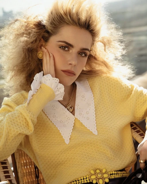 Blonde woman in yellow sweater with white collar, gold jewelry posing outdoors in golden light, fashion editorial portrait, close up.