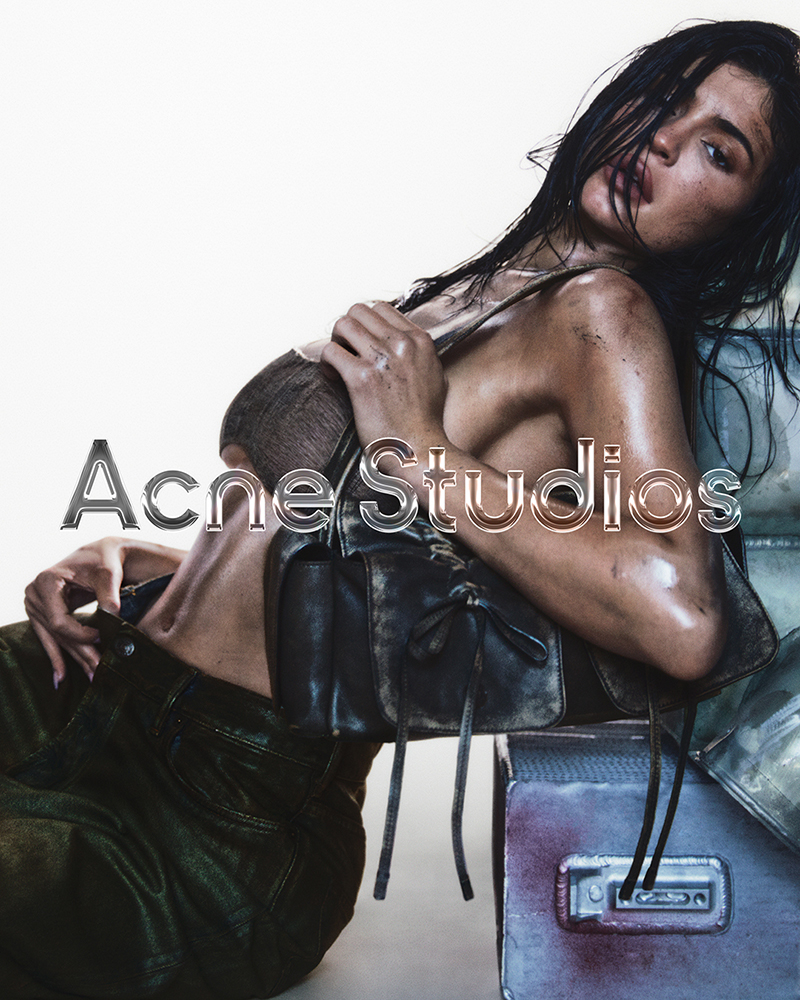 Adult woman poses indoors with a leather bag and leather pants. The text 'Acne Studios' is visible in the center of the frame.
