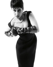 Model in black dress wearing pearl necklace and glossy textured gloves against plain white background