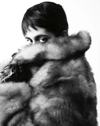 Close-up portrait of a model with short dark hair wearing a fluffy fur collar coat, styled by Peter Simon Phillips.