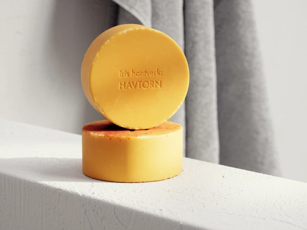 Two round bars of yellow soap stacked on a white surface against a light background with a grey towel partially visible.