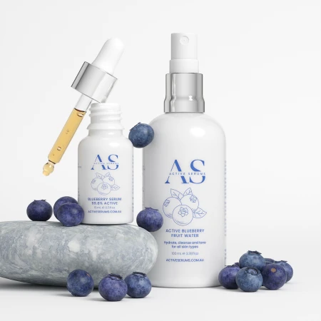 Product shot of AS Active Serums Blueberry Serum and Active Blueberry Fruit Water, staged with fresh blueberries and a grey stone.
