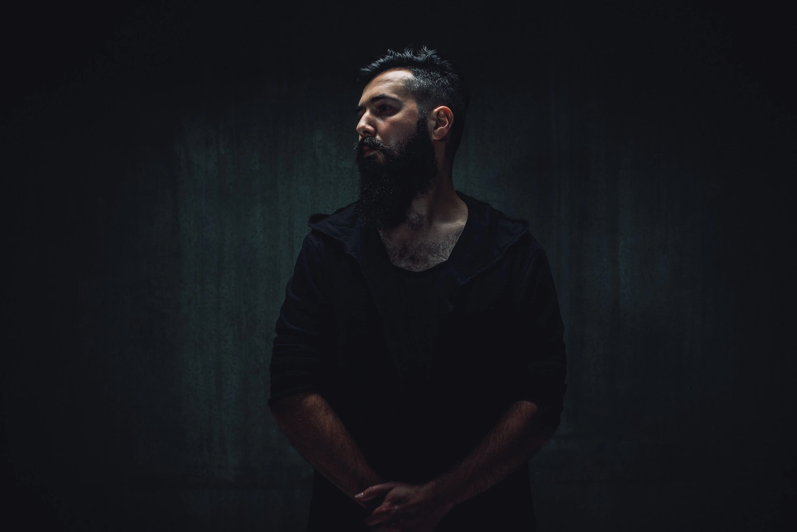 Portrait of a bearded man in a black hooded sweatshirt against a dark textured background shot by Wren Steiner