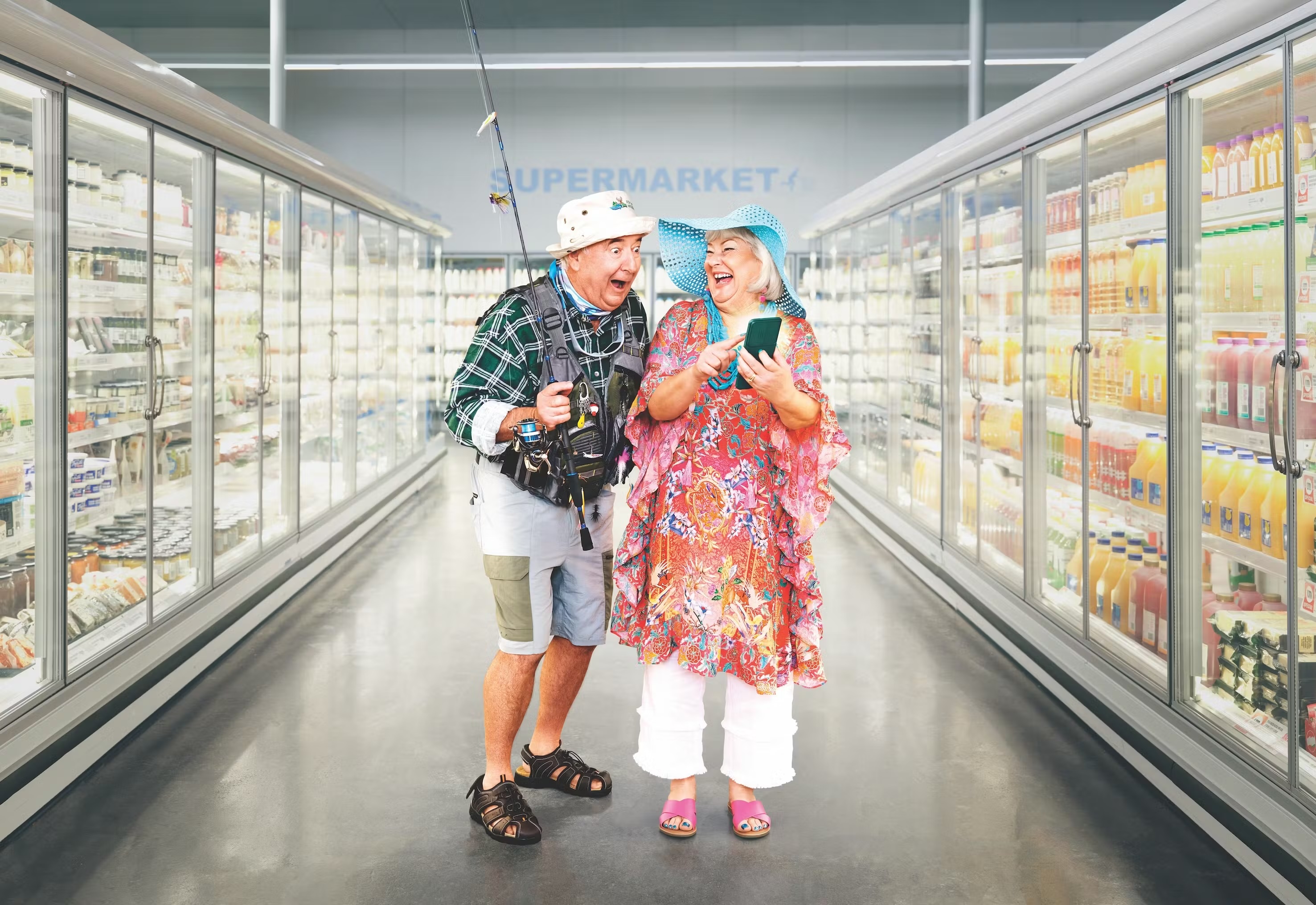 Elderly couple in a supermarket aisle, woman using a phone, man holding a fishing rod, creating a humorous, lifestyle scene.
