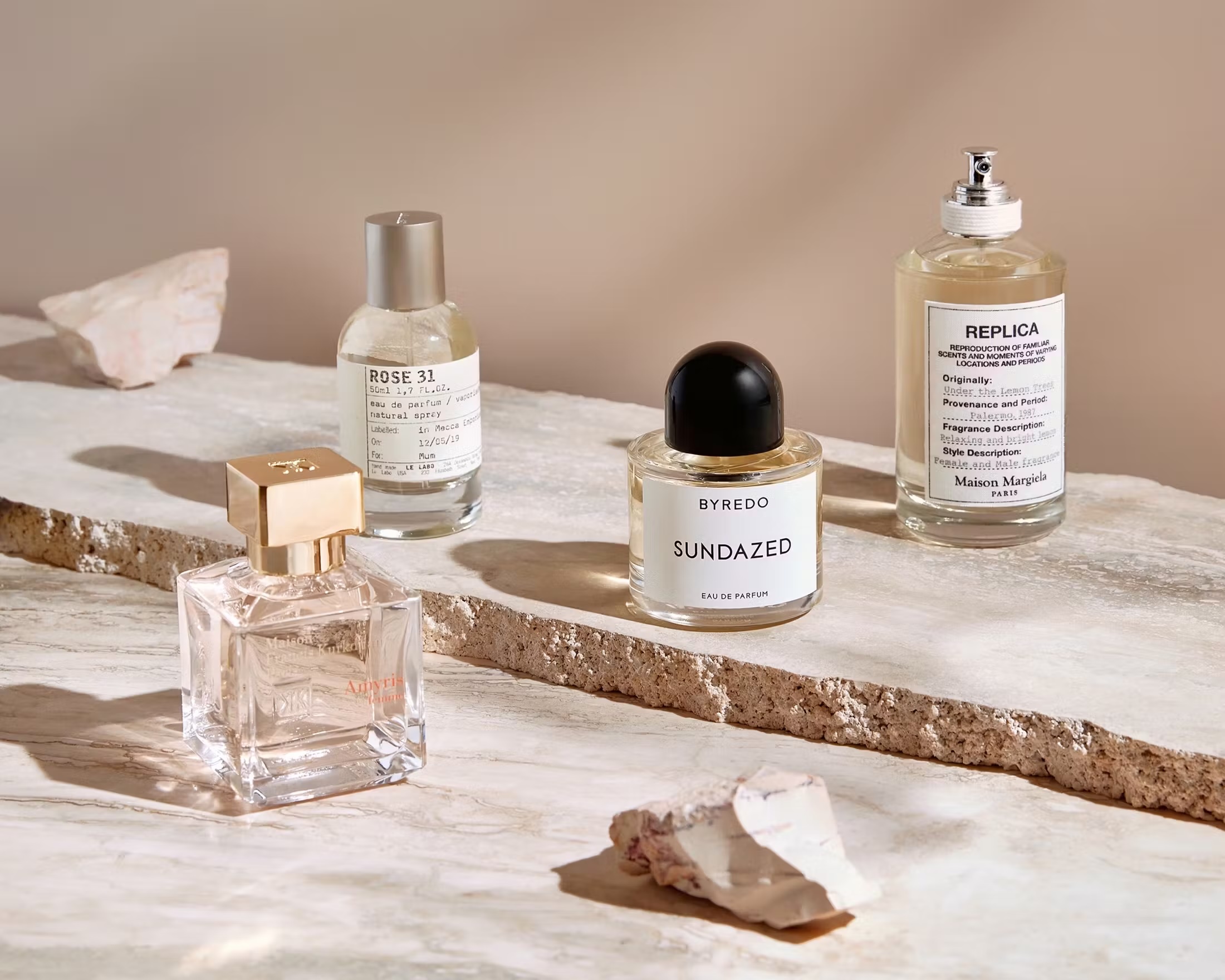 Four perfume bottles sit on a marble surface with scattered rocks, creating an elegant and minimalist fragrance product display.