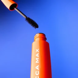 Orange mascara tube being opened with brush wand pulled out against vibrant blue background