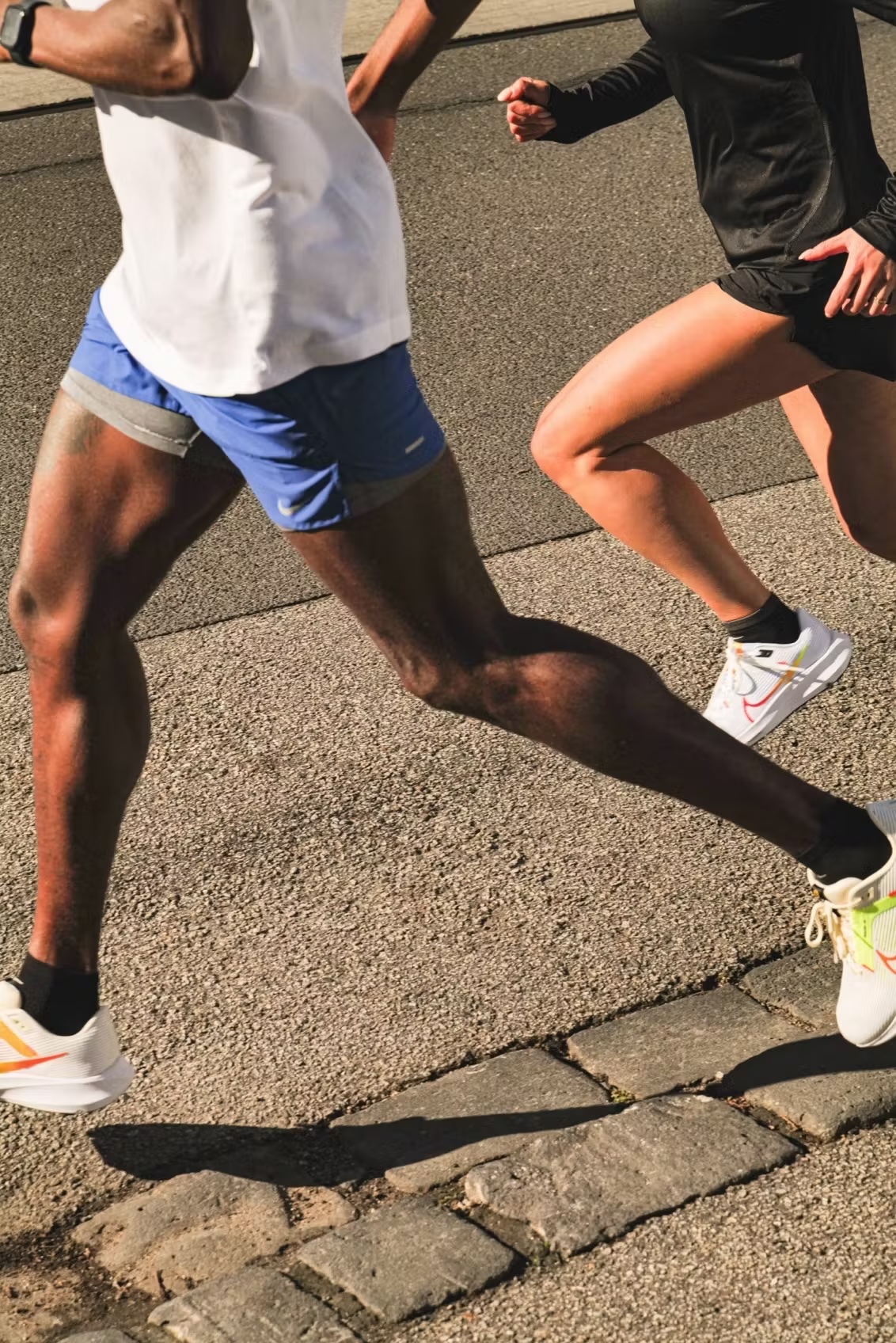 Two athletes in sportswear running on a paved surface, showcasing fitness and healthy lifestyle in natural daylight, action shot.