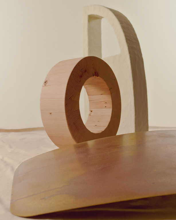 Abstract geometric art installation with circular wood element, arch, and reflective surface against a neutral background.