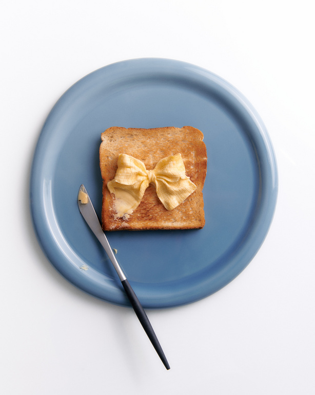 Toast with butter bow tie on a blue plate next to a butter knife, flat lay food photography, minimal composition, food presentation.