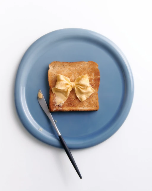 Toast with butter bow tie on a blue plate next to a butter knife, flat lay food photography, minimal composition, food presentation.