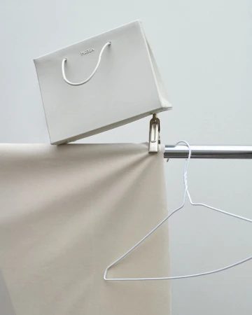 Still life of a white paper shopping bag hanging from a metal clip on a clothing rack with a metal wire hanger, studio lighting.