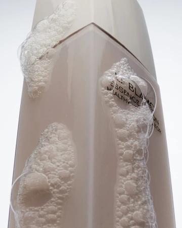 Close-up of a white skincare bottle with bubbles clinging to the surface, label visible, in a clean, well-lit studio setting.