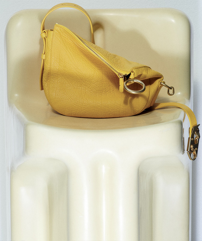 Yellow leather handbag with silver hardware sits on a white chair in a close-up studio product shot, showcasing its texture and design.