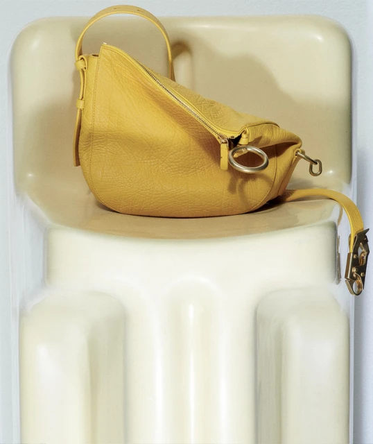 Yellow leather handbag with silver hardware sits on a white chair in a close-up studio product shot, showcasing its texture and design.