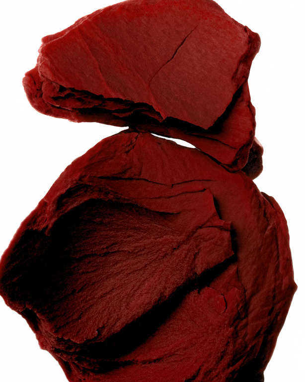 Close-up studio shot of stacked, rough-textured, burgundy-colored shale fragments against a bright white background.