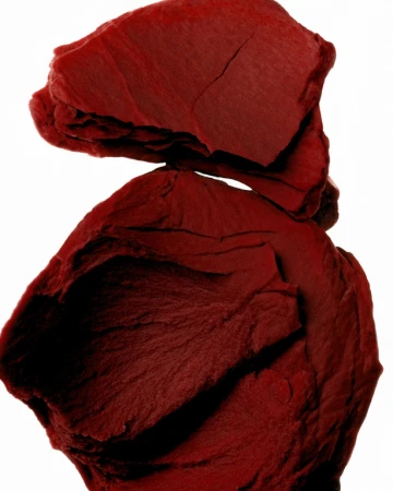 Close-up studio shot of stacked, rough-textured, burgundy-colored shale fragments against a bright white background.