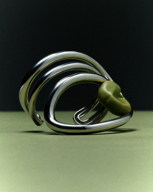 Abstract view of a silver-tone metal bangle bracelet with curved elements, paired with a green bean, set against a dark background.