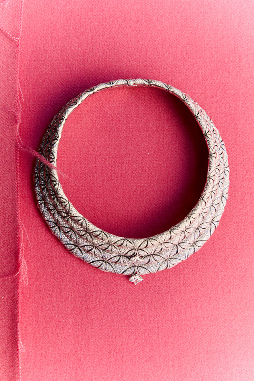 Elegant silver choker necklace with intricate floral details and a central diamond pendant against a vibrant pink backdrop.