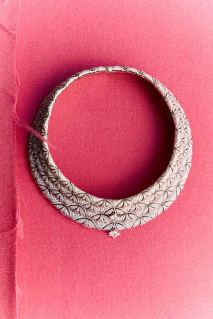 Elegant silver choker necklace with intricate floral details and a central diamond pendant against a vibrant pink backdrop.