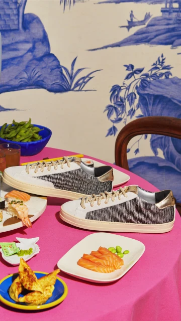 Two sneakers and plates of appetizers are arranged on a pink tablecloth, set against a blue and white toile wallpaper backdrop.