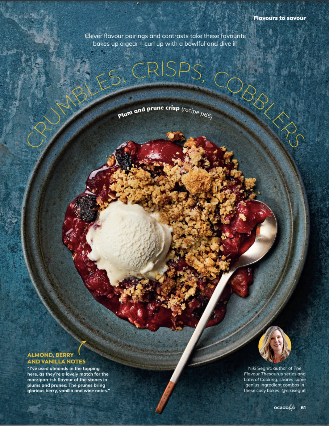 Overhead shot of plum and prune crisp with vanilla ice cream in a blue bowl, accompanied by a spoon on a mottled blue surface.